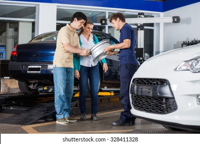 Male technician and couple examining metallic alloy at garage