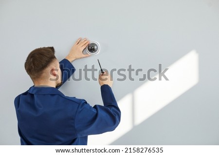Male technician installing surveillance camera on light copy space wall. Back view of repair service worker using screwdriver to fit screws and adjust wall mounted CCTV security dome cam inside house