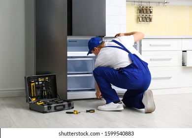 Male Technician Repairing Broken Refrigerator In Kitchen