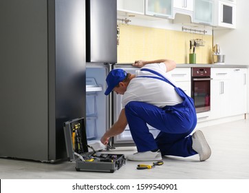 Male Technician Repairing Broken Refrigerator In Kitchen