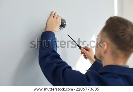 Male technician repairing modern security camera. Maintenance service worker uses screwdriver to fit screws and adjust wall mounted CCTV surveillance dome video cam at home or inside office building