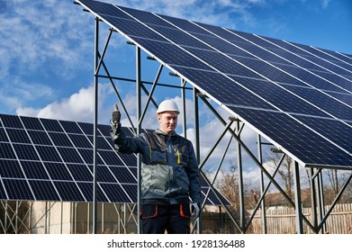 Männlicher Techniker, der eine Genehmigungsgeste zeigt, hält sich während seines Stehens in der Nähe der Fotovoltaik-Anlage auf. Elektriker, der alternative Energiequellen genehmigt. Konzept der Macht nachhaltige Ressourcen.