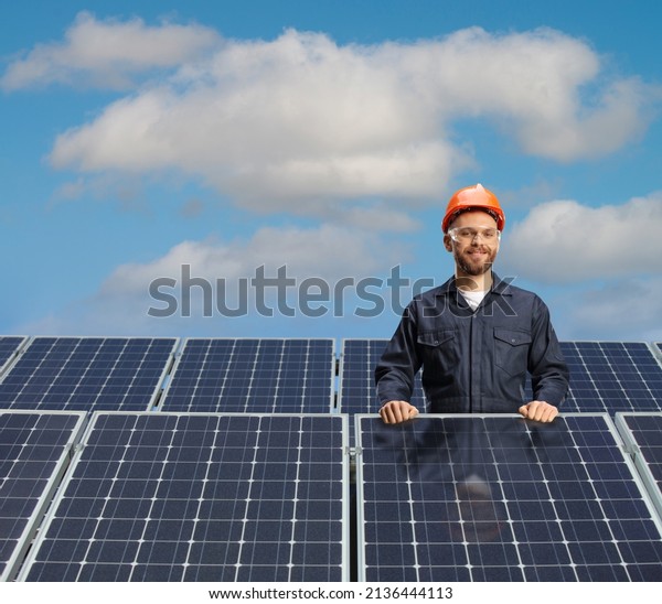 Male technician in a uniform posing behind solar\
cells on a roof