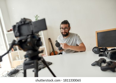 Male Technology Blogger Holding, Pointing At Headphones While Recording Video Blog Or Vlog About New Gadgets At Home Studio. Blogging, Work From Home Concept. Horizontal Shot