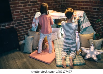 Male Teen Helping Little Sister Prepare A Makeshift Tent For Sleepover