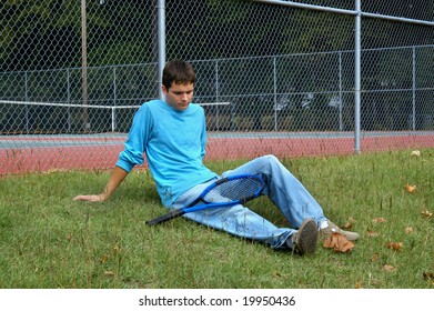 Male Teen Sits Outside The Tennis Courts Dejected And Discouraged.  Sidelined With Injury And Unable To Play.