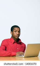 Male Teen Student Looks At The Camera With A Serious Expression As He Works On His Laptop Computer. Vertically Framed Photograph