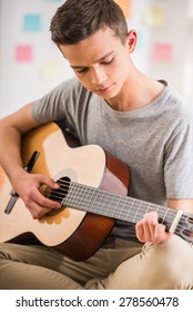 Male Teenager Sitting At Home And Playing Guitar.