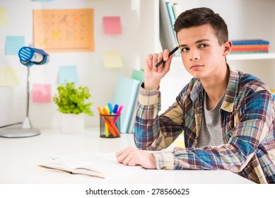Male teenager sitting at the table and holding a pen in hand and thinking.