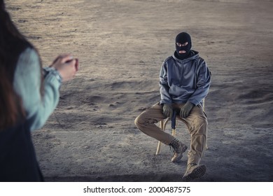 Male Terrorist Sitting On Chair Against Female Hostage Outdoors