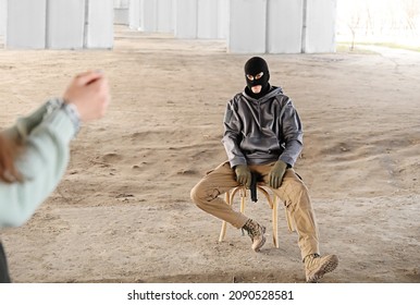 Male Terrorist Sitting On Chair Against Female Hostage Outdoors