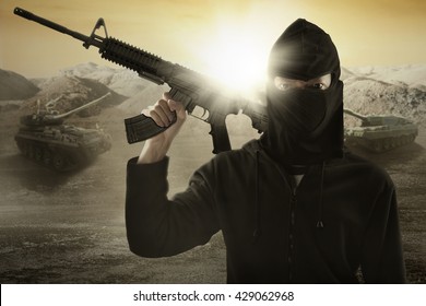 Male terrorist wearing mask and holding a machine gun with military vehicle background