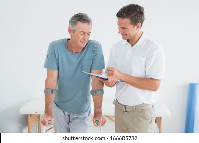 Male therapist discussing reports with a disabled patient in the gym at hospital - Powered by Shutterstock