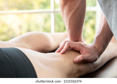 Male therapist giving leg and calf massage to athlete patient on the bed in clinic, sports physical therapy concept