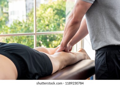 Male Therapist Giving Leg Massage To Athlete Patient On The Bed In Clinic, Sports Physical Therapy Concept