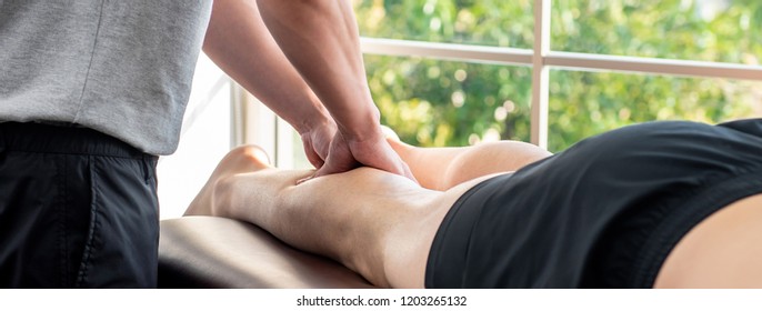 Male therapist giving leg massage to athlete patient on the bed in clinic for sports physical therapy concept, banner proportion