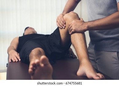 Male therapist massaging knee of athlete patient - sport physical therapy concept