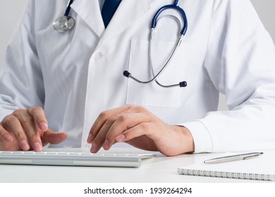 Male Therapist Typing At Wireless Computer Keyboard. Physician In Medical Uniform With Stethoscope Working With Computer At Desk. Modern Technology In Examination And Diagnosis. Health Care Concept