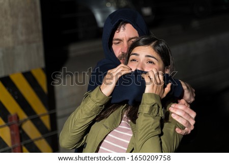 Male thief assaulting female victim while covering her mouth in dark alley