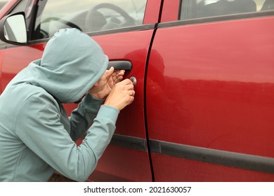 A Male Thief In A Hood Is Trying To Get Into A Car Without An Alarm. A Burglar Breaks The Door Lock Of A Private Vehicle.