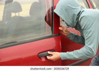 A Male Thief In A Hood Is Trying To Get Into A Car Without An Alarm. A Burglar Breaks The Door Lock Of A Private Vehicle.