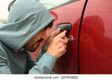 A Male Thief In A Hood Is Trying To Get Into A Car Without An Alarm. A Burglar Breaks The Door Lock Of A Private Vehicle.