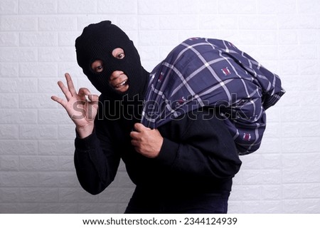 Male thief sneaking away with a bag while showing okay hand gesture 
