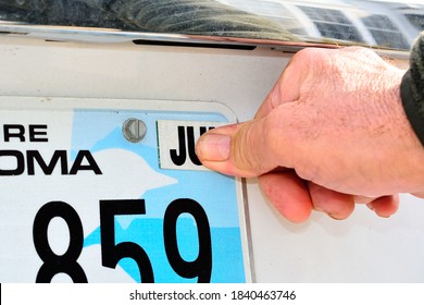 A male thumb pressing the required month tag for an annual license registration on rear license plate.