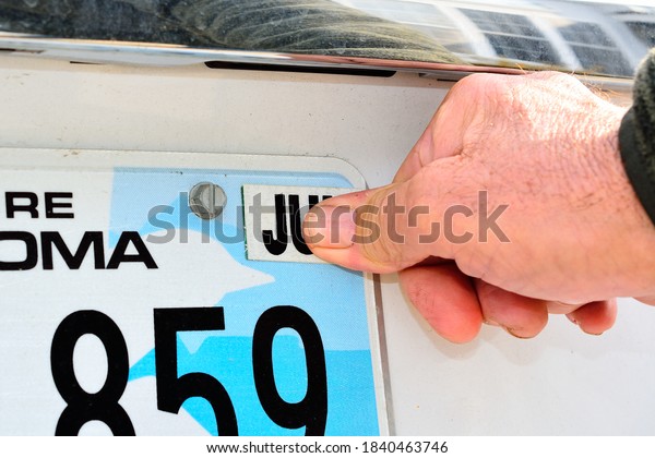 A male thumb pressing\
the required month tag for an annual license registration on rear\
license plate.