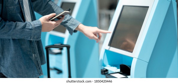Male tourist holding passport and smartphone using self check-in kiosk in airport terminal. Travel abroad concept