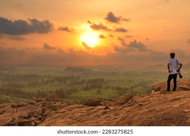 Male tourist photographer enjoys a scenic sunset view from a hill top at Hampi, Karnataka, India - Powered by Shutterstock