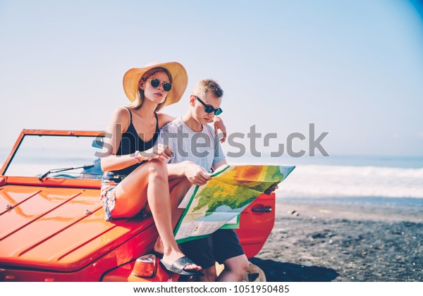 Male tourist reading map for checking direction\
traveling with girlfriend on summer vacation renting convertible\
automobile, romantic couple in love making stop on ocean shore\
planning route