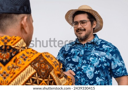 A male tourist shakes the hand of a local indonesian man in a batik shirt. Isolated on a white background.