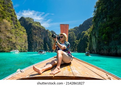 Male tourist taking pictures at the prow of a long-tail boat on a tropical island, Koh Lipe, Andaman Sea, Thailand.