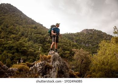 male tourist with trekking poles and backpack stands on hill against background of mountains of Turkey
