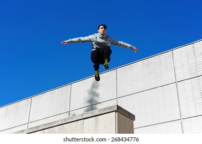 Male tracer free runner jumping forward from high rooftop over beautiful blue sky background, young tracer athlete jumping over building roof at sunny day - Powered by Shutterstock