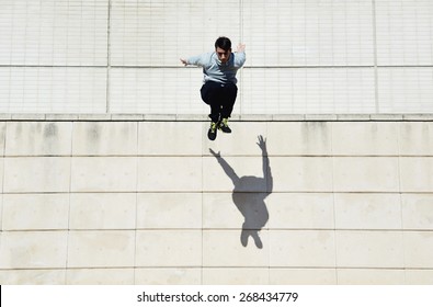 Male tracer free runner jumping forward from high rooftop over cement building background, young tracer athlete jumping over building roof at sunny day - Powered by Shutterstock