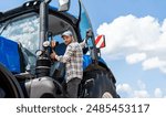 Male  tractor driver gets into the blue farm tractor.