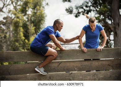 Male trainer assisting woman to climb a wooden wall during obstacle course - Powered by Shutterstock