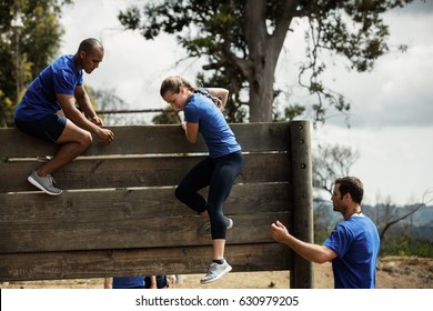 Male trainer assisting woman to climb a wooden wall during obstacle course - Powered by Shutterstock