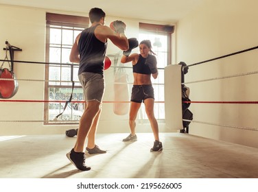 Male trainer helping young female boxer with striking techniques in a boxing ring. Young boxing coach training a young woman in a gym. - Powered by Shutterstock