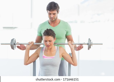 Male Trainer Helping Young Fit Woman To Lift The Barbell Bench Press In The Gym