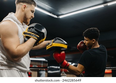 A male trainer helps a teenage boxer with striking techniques in a boxing ring. - Powered by Shutterstock