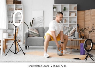 Male trainer with kettlebell recording sports video on phone at home - Powered by Shutterstock