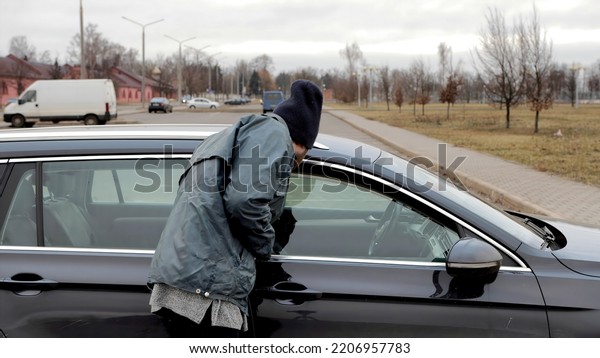 Male tramp bum looks through\
slightly open window of auto\'s door and walks away. Vehicle with\
alarm system. Property insurance against theft crime.\
Beggar.