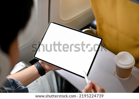 Male traveler or passenger sits at the window seat, using his portable digital tablet touchpad during the flight. tablet white screen mockup. close-up image
