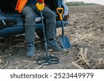 A male treasure hunter sits in the trunk of his car leaning on a metal detector.