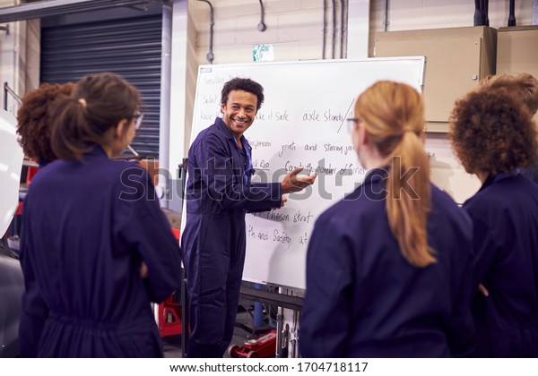 Male Tutor By Whiteboard With\
Students Teaching Auto Mechanic Apprenticeship At\
College