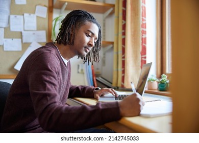 Male University Or College Student Studying With Laptop At Desk In Room