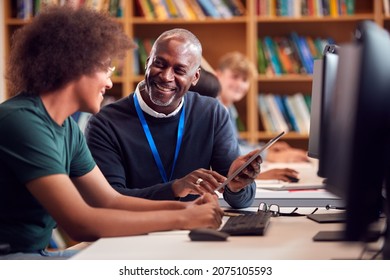 Male University Or College Student Working At Computer In Library Being Helped By Tutor